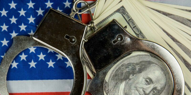 handcuffs used in a false arrest lays on top of the settlement money and flag