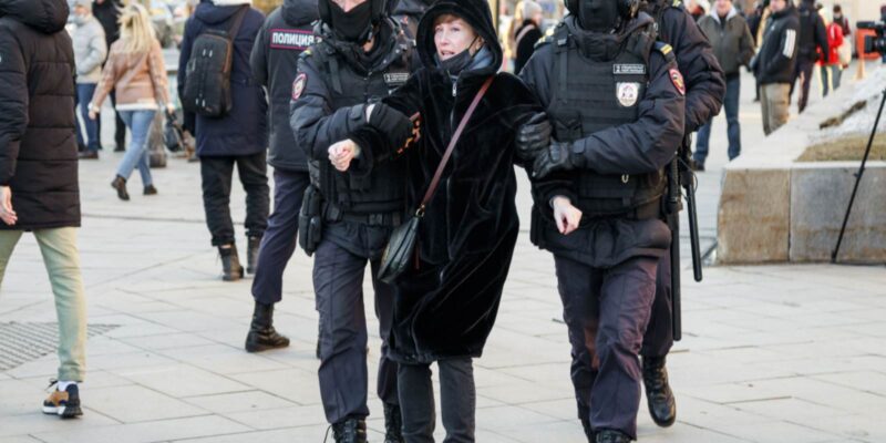 Two police officers are detaining a woman in a market