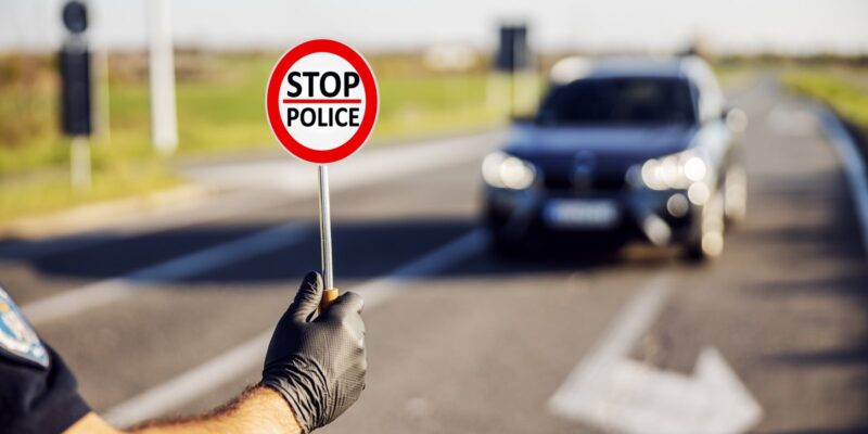 A policeman is showing a signboard to the car that says 'stop police'