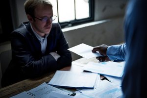 An attorney examining documents in a dark room while someone is giving him an envelop